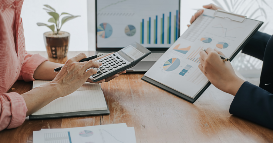 Two people at a wooden desk reviewing financial charts and graphs, one using a calculator.