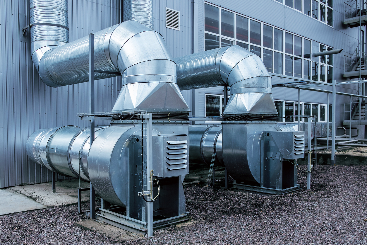 Industrial ventilation system with large metal exhaust and intake ducts installed outside a manufacturing facility.