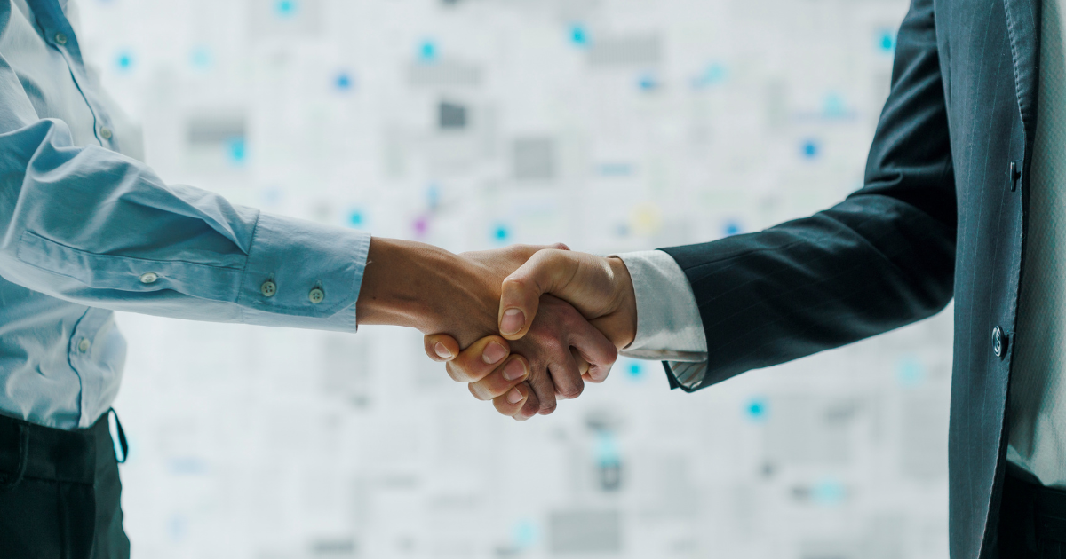 Two business professionals shaking hands in front of a blurred background of documents