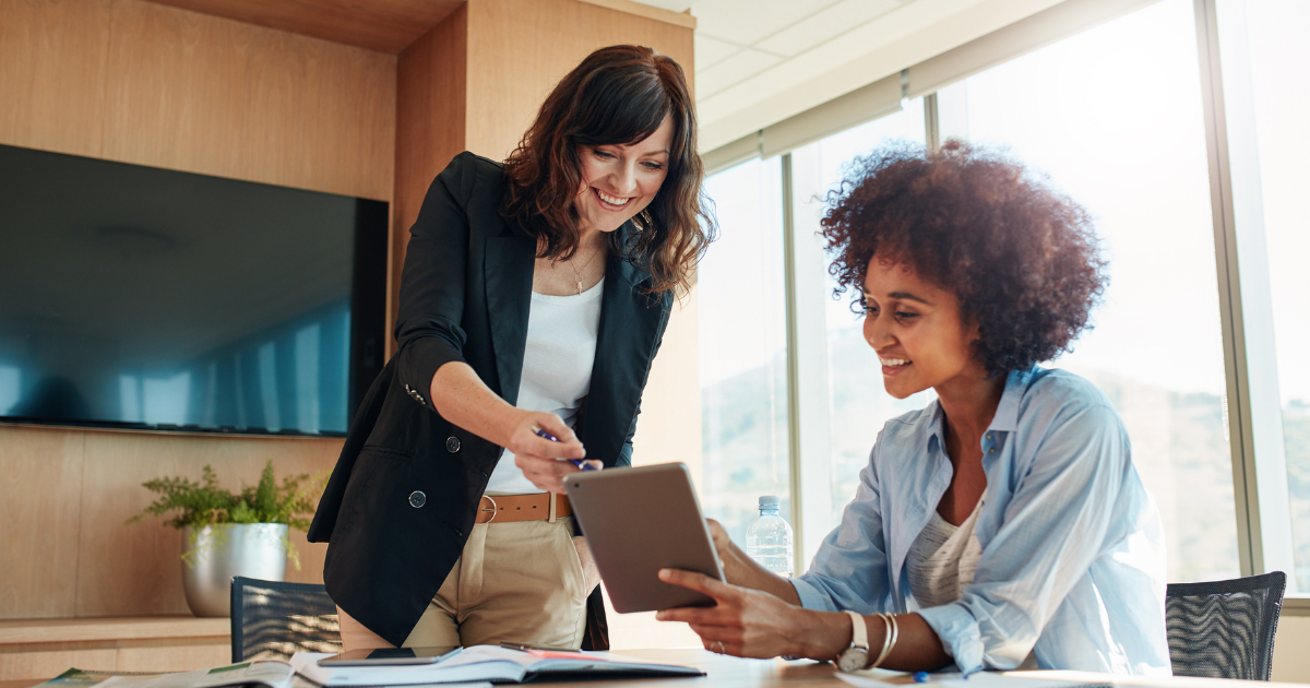 Two business partners smiling as they review information on a tablet in a bright office