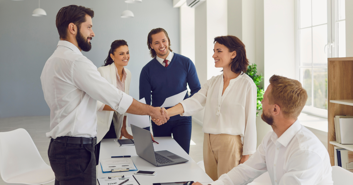 Business partners shaking hands at a conference table while colleagues look on and smile